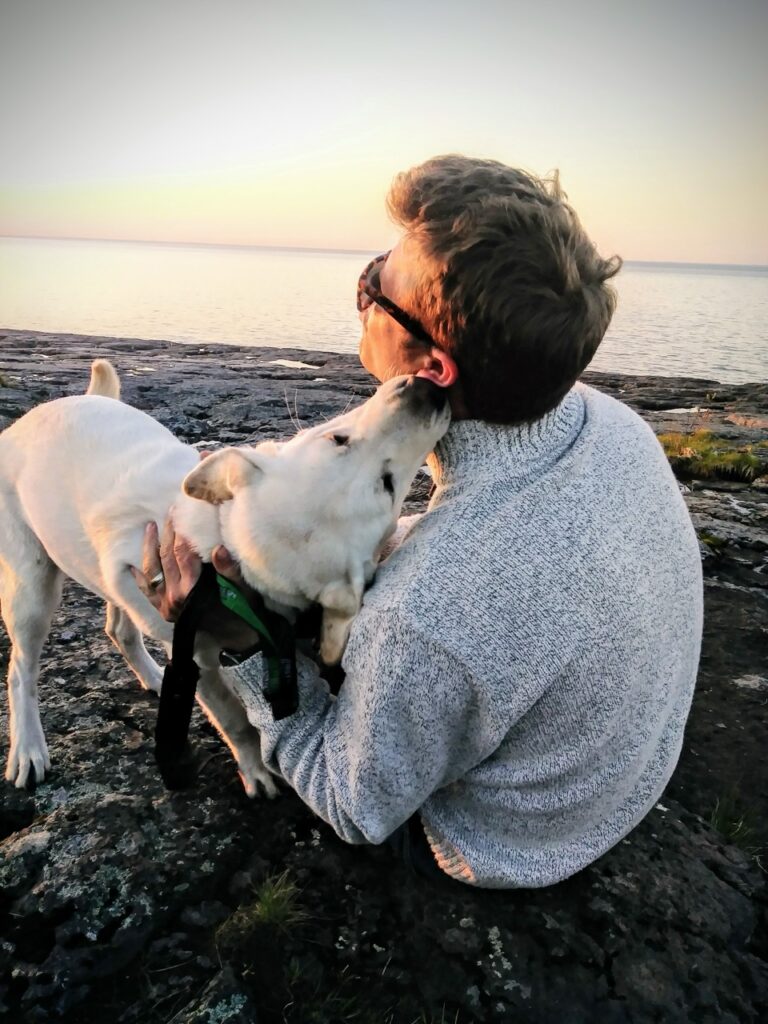 side-view-man-with-dog-sitting-rock-beach-against-sky-sunset-Large